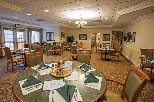 Spacious dining room with several round and rectangular tables set with green napkins and menus.