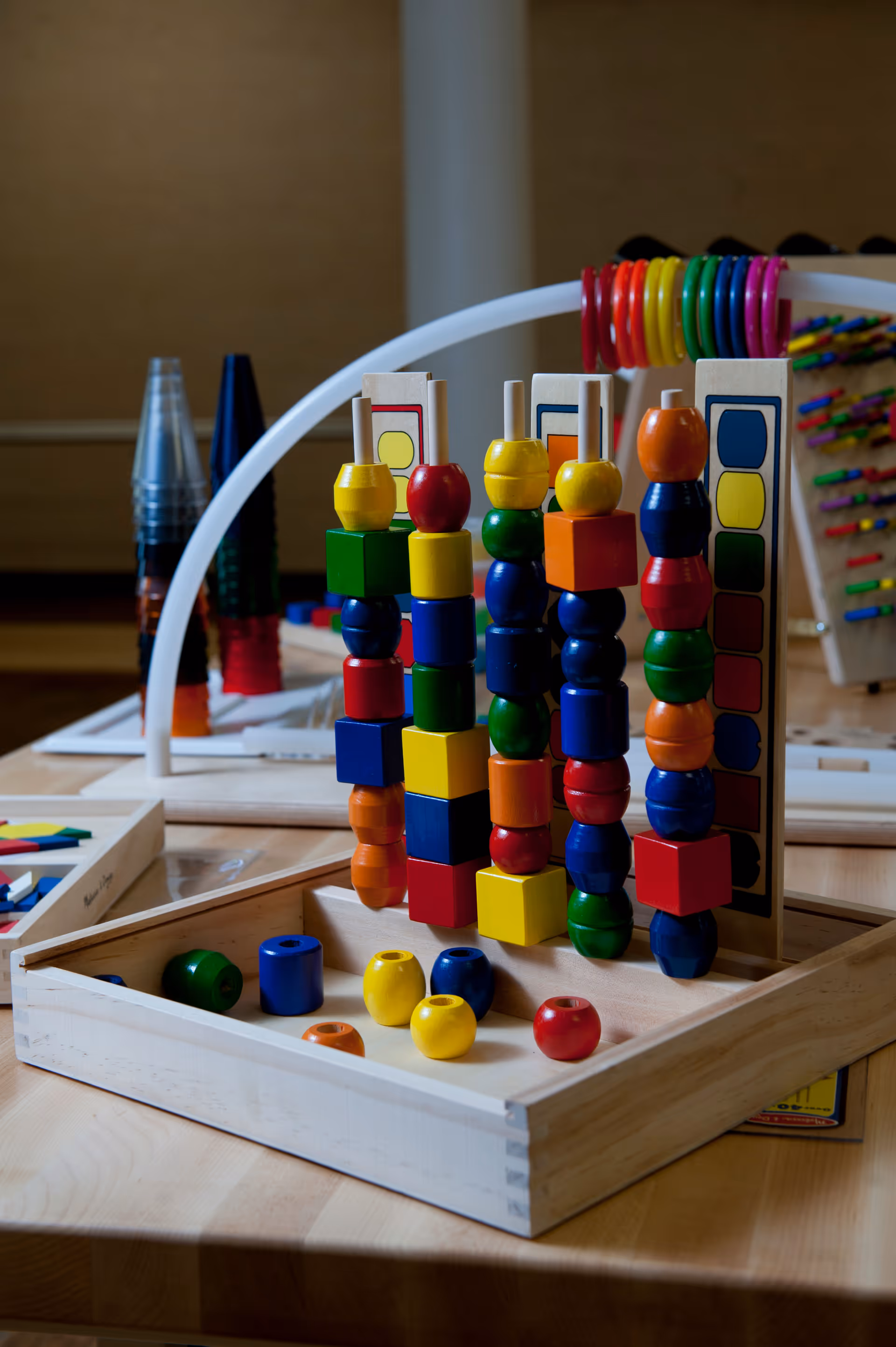 A wooden activity toy with colorful beads and blocks arranged on vertical pegs on a table.