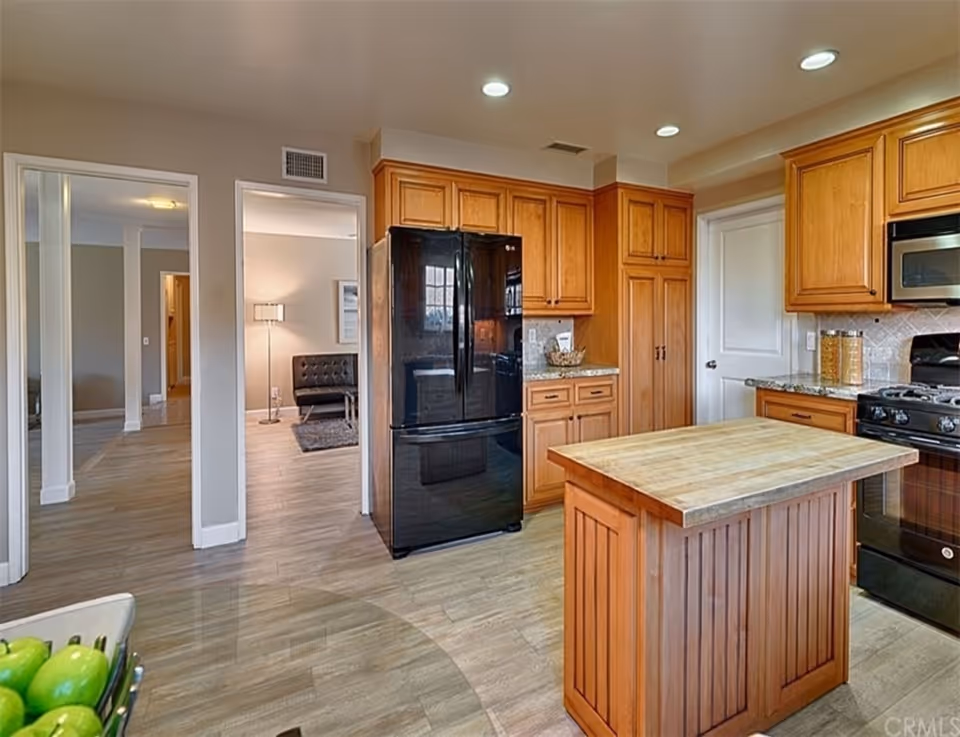 Bright kitchen with wooden cabinets, central island, and black refrigerator.