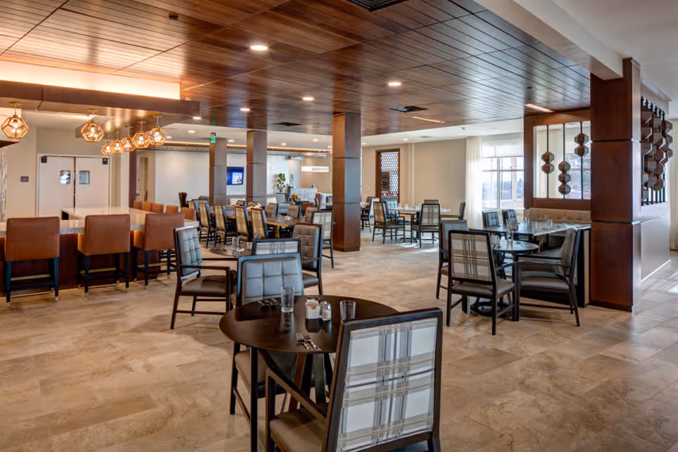Spacious modern dining room with multiple tables and chairs, a bar with pendant lights, and a wood-accent ceiling.