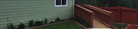 Green building exterior with a wooden ramp and railing beside a red fence.