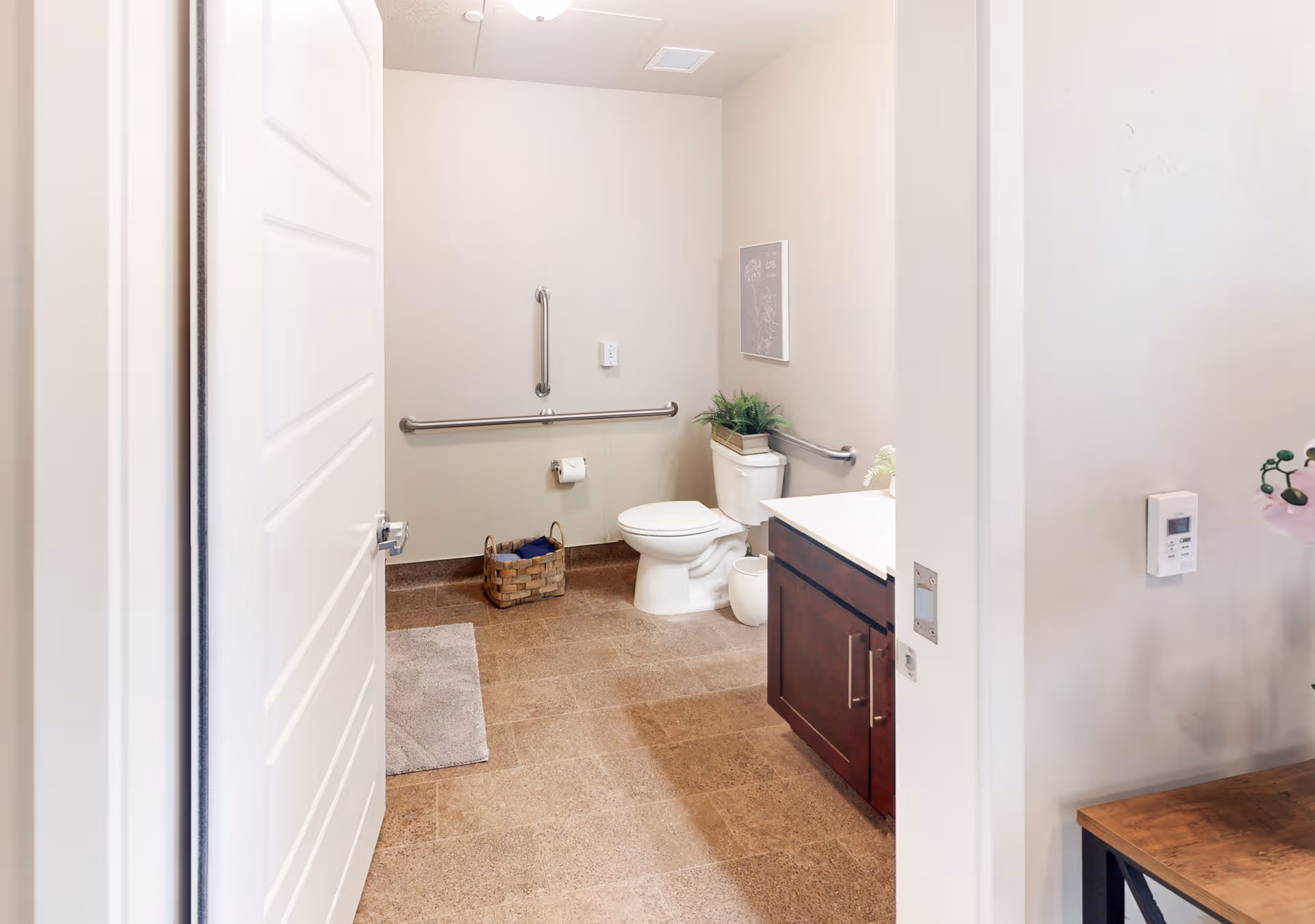 Accessible bathroom with a toilet, wall grab bars, vanity sink, and a basket on the tiled floor.
