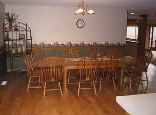 Communal dining room with a long wooden table, several wooden chairs, hardwood floors, and a small chandelier.