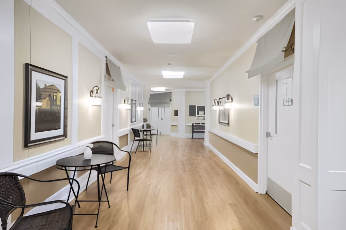 Well-lit interior corridor with small bistro tables and chairs, wall sconces, and framed artwork.