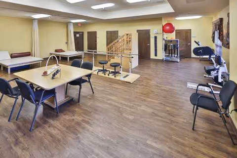 Spacious therapy room with parallel bars, exercise equipment, a red exercise ball, and seating.