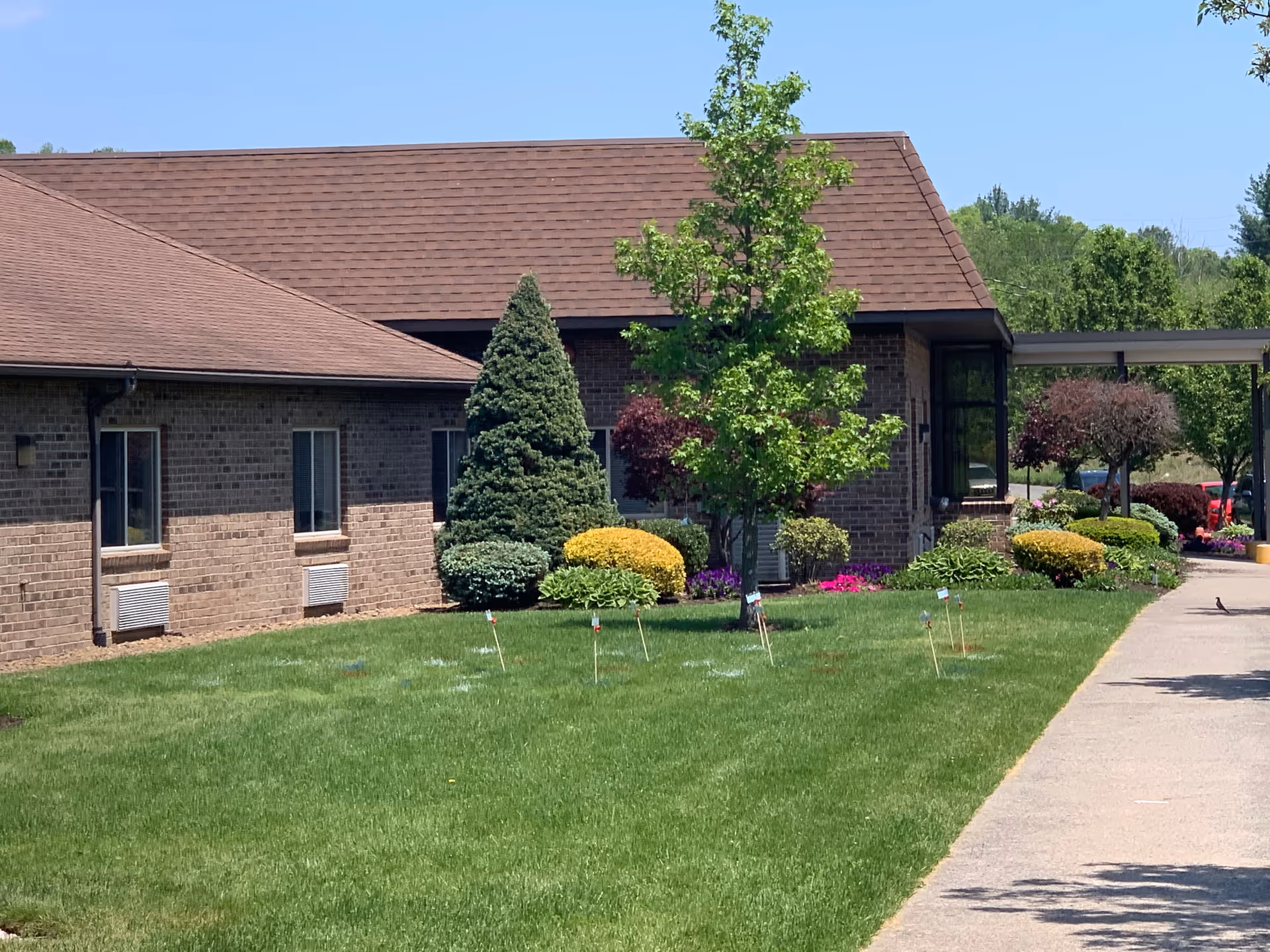 Brick building front with a manicured lawn, shrubs, trees and a sidewalk leading to a covered entrance.