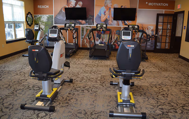 Exercise room with recumbent bikes and treadmills facing TVs and motivational wall graphics.