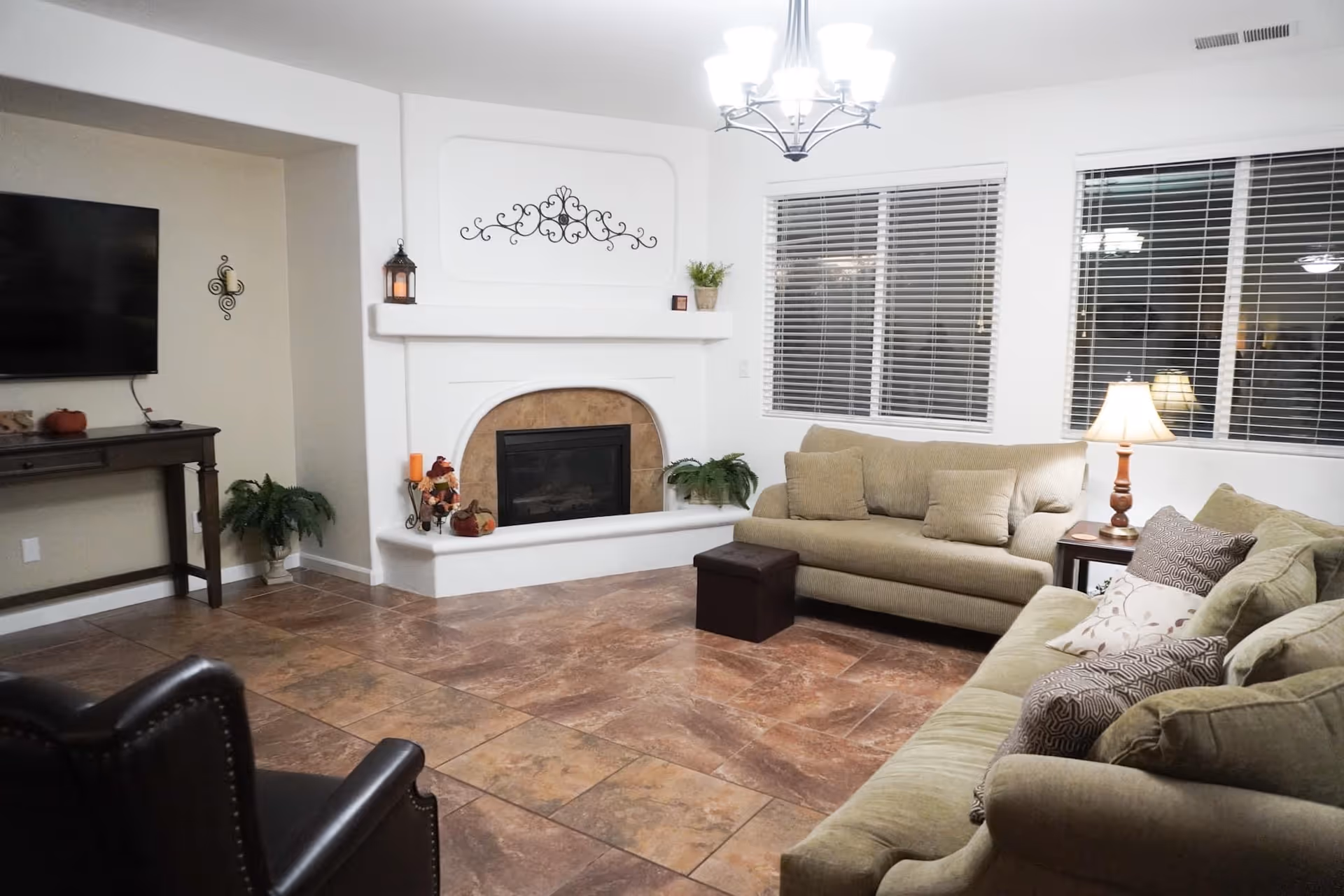 Cozy living room with two sofas, a fireplace, a wall-mounted TV, and large windows with blinds.