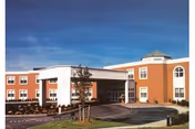 Front exterior of a two-story brick senior living facility with a covered entrance, circular driveway, and landscaped lawn under a blue sky.