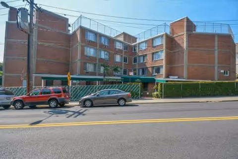 Brick multi-story nursing facility with green canopy entrance and cars parked along the street.