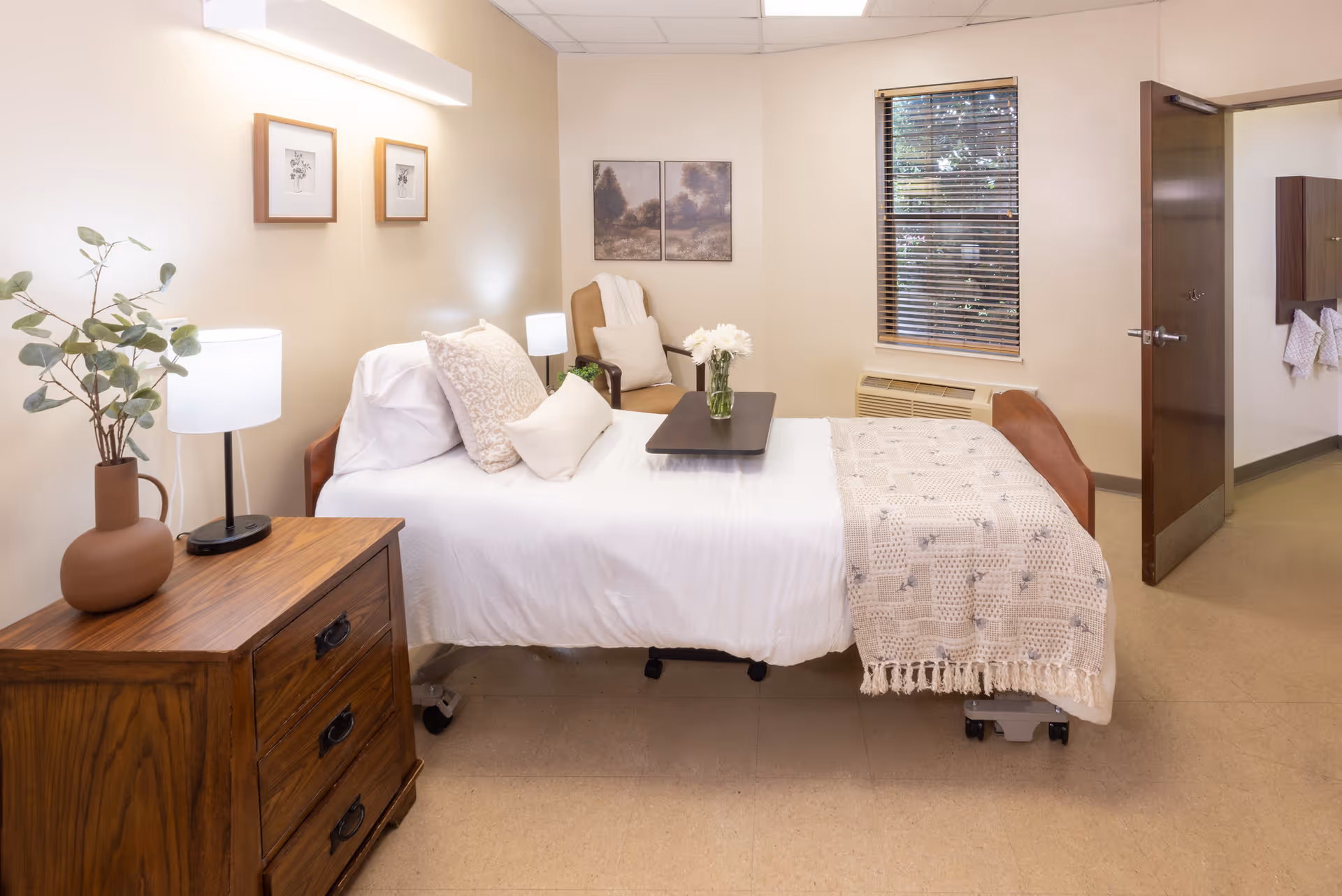 Neatly staged senior living bedroom with a single bed, bedside table, lamp, armchair and window.