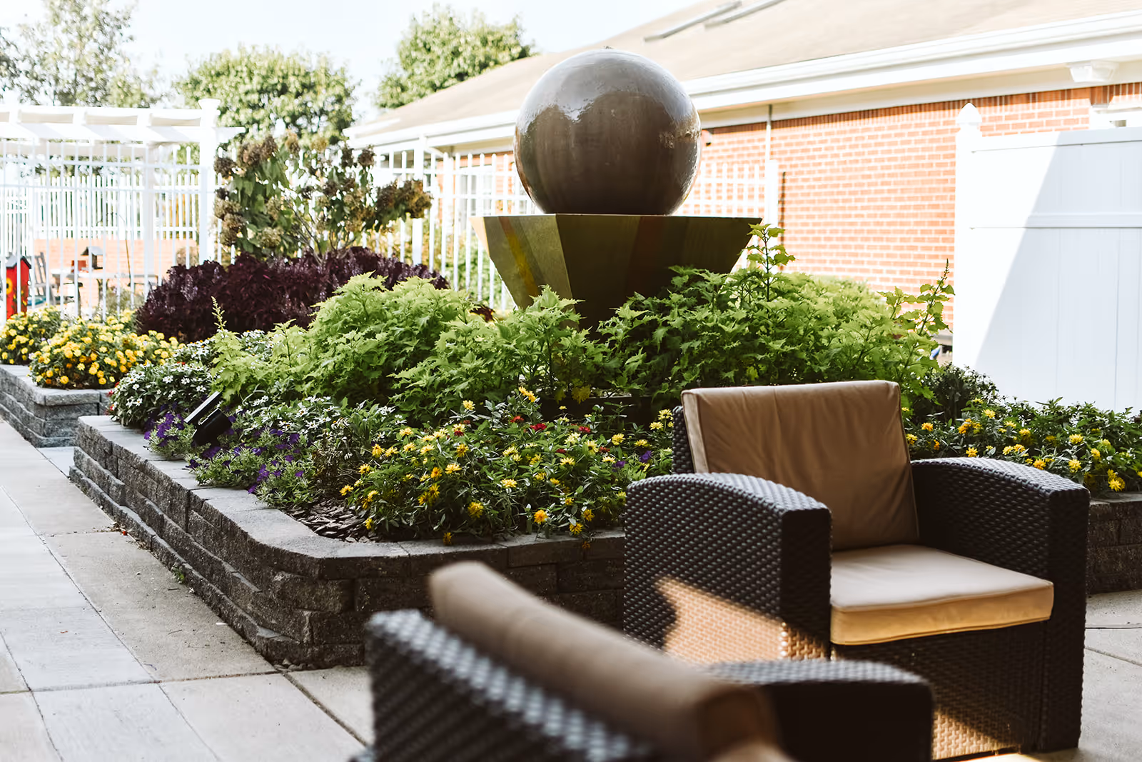 Outdoor courtyard with raised flower beds, a spherical water fountain, and wicker patio chairs.