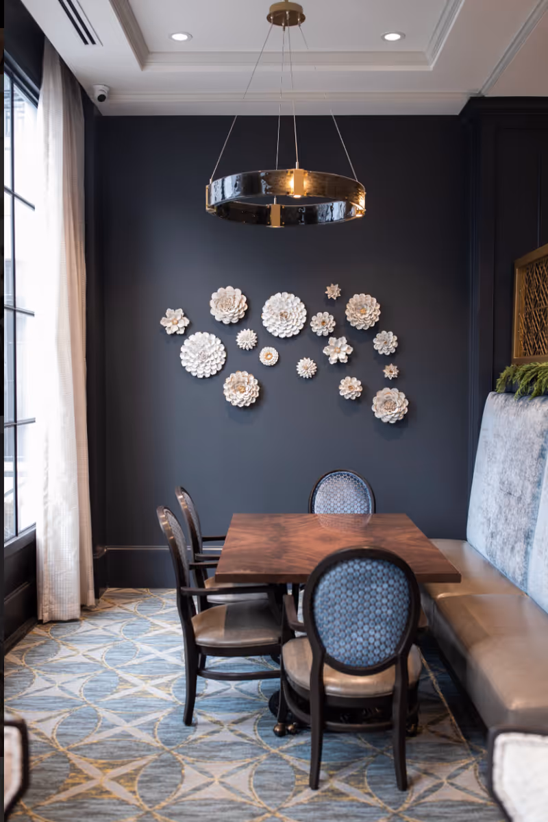 Elegant dining nook with a wooden table, upholstered chairs and banquette under a ring pendant and decorative ceramic wall flowers.