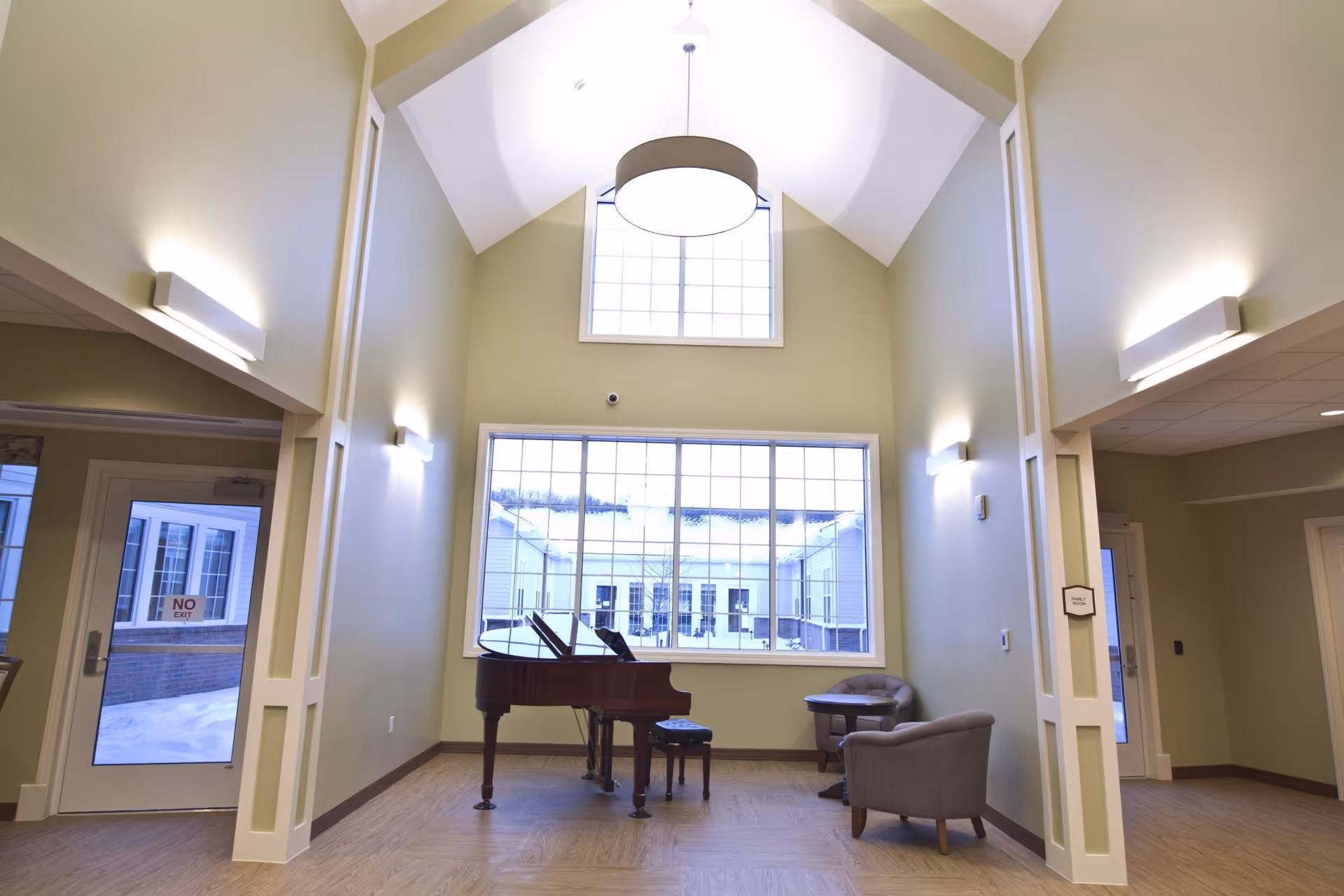 Bright high-ceiling common room with a grand piano and seating in front of large windows.