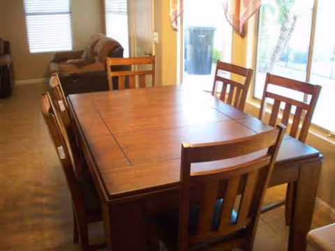 Wooden dining table with six chairs in a bright senior living dining room.