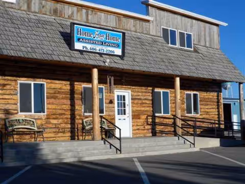 Log-style assisted living building with front steps, benches, and a sign.