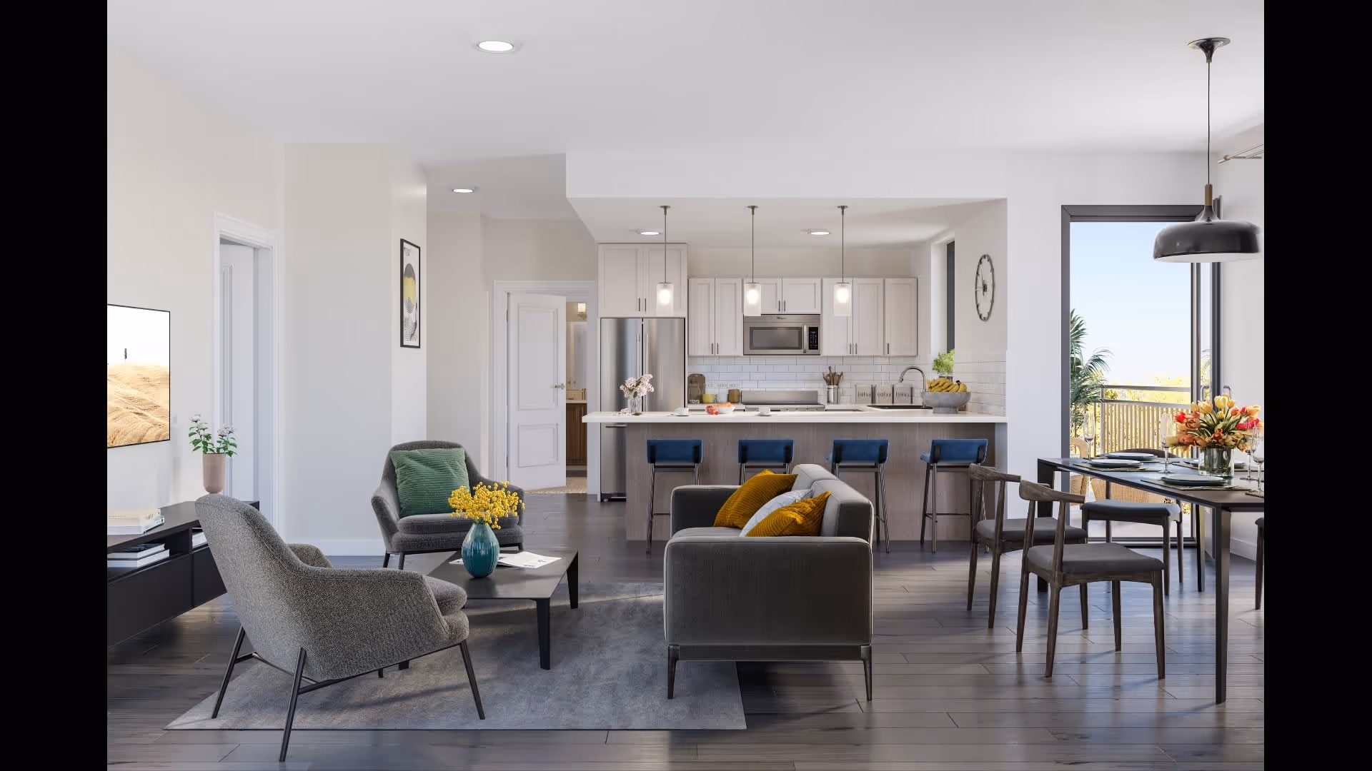 Modern open-concept living space featuring a living room with gray armchairs, a gray sofa with yellow pillows, a coffee table with a vase of yellow flowers, and a TV mounted on the wall. The space opens into a kitchen with white cabinets, stainless steel appliances, a large island with four blue bar stools, and pendant lighting. Adjacent to the kitchen is a dining area with a table set for four and a large window showing an outdoor balcony with greenery.