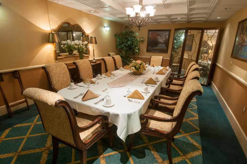 Elegant private dining room with a long set table, upholstered chairs, chandelier, and place settings.