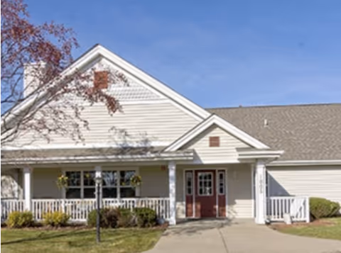 Front exterior of a single-story building with a covered porch, double red entrance doors, and a small lawn and walkway.