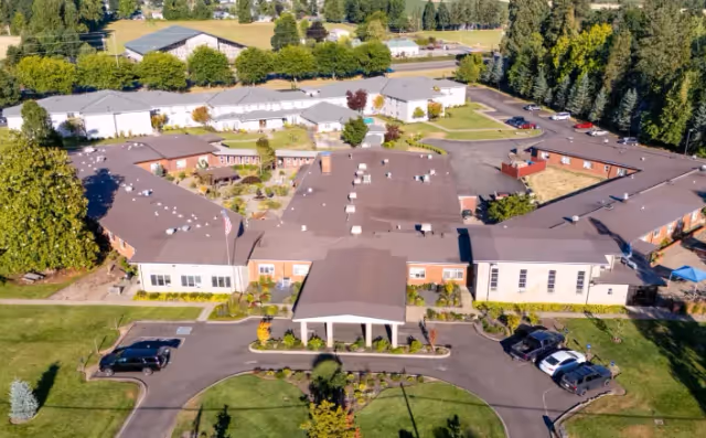 Aerial view of Mt. Angel Orchard House senior living campus with a central entrance canopy, connected wings, parking lots, and well-kept landscaping.