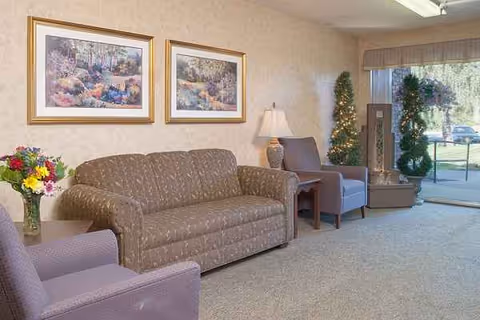 A cozy senior living lounge with sofa, chairs, wall art, and a glass door to outdoors.