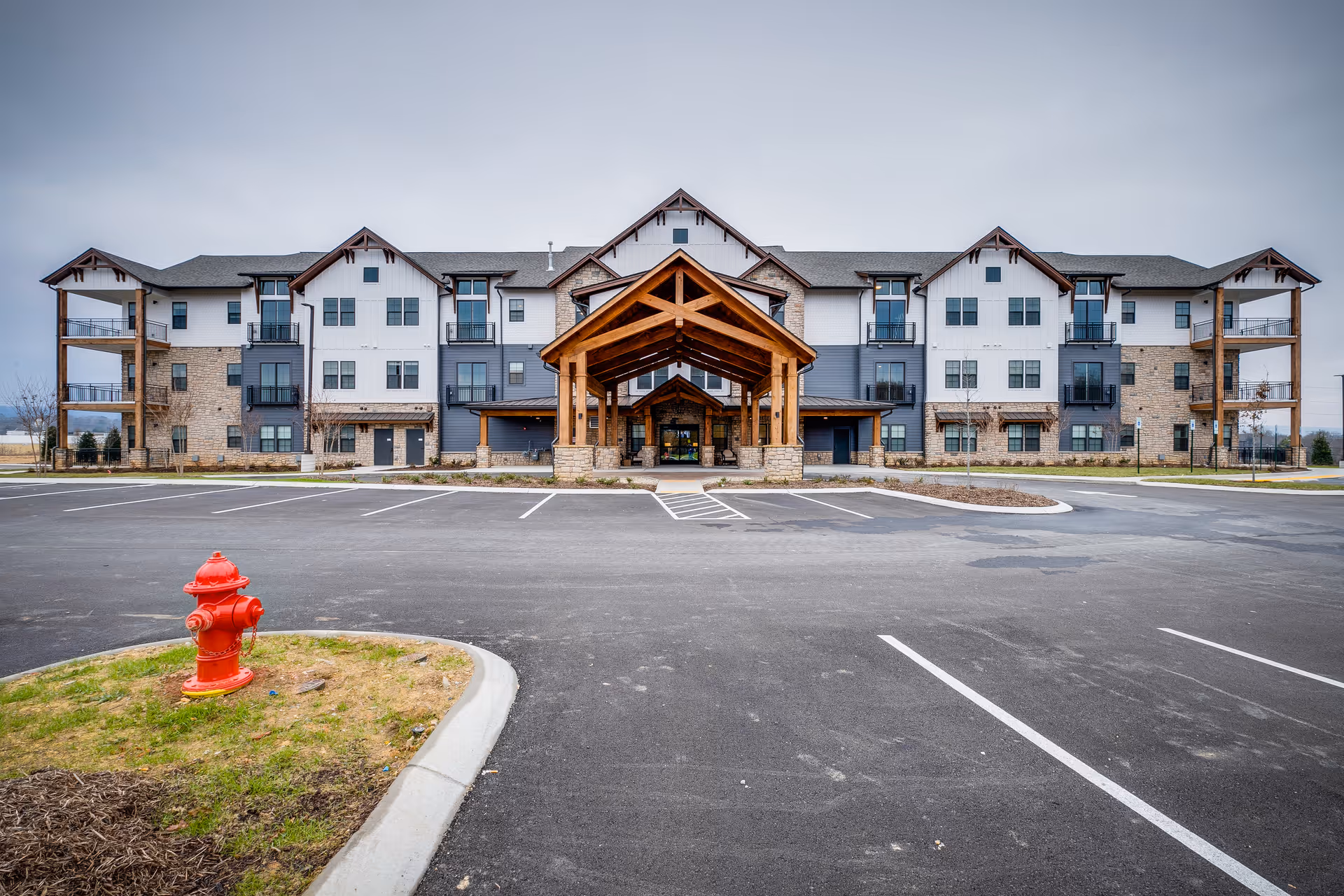 Front exterior view of a large, modern senior living facility named Everlan of Hixson with a spacious parking lot and a red fire hydrant in the foreground under a cloudy sky.