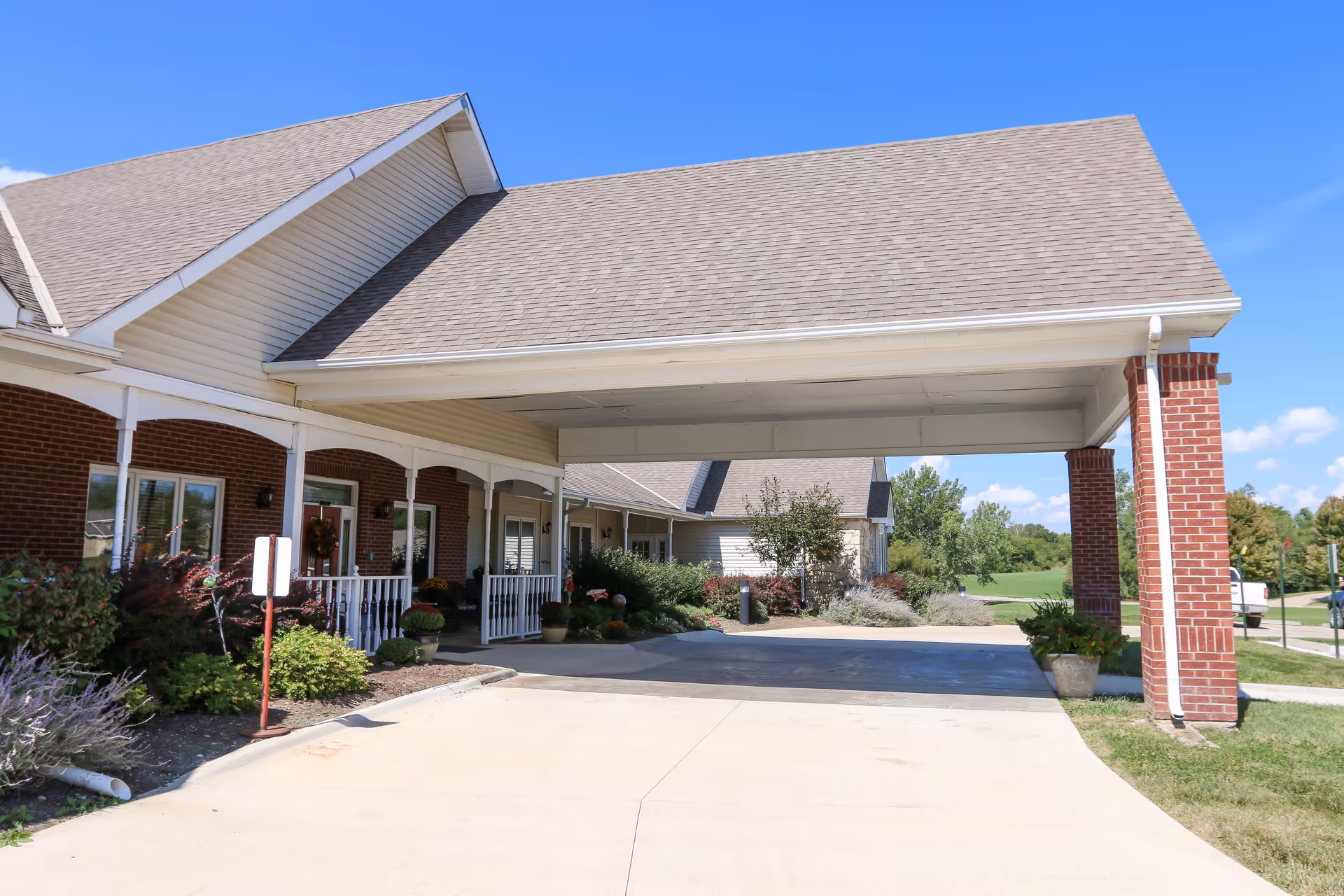 Covered porte-cochère entrance of a brick senior living building with a driveway and landscaping.