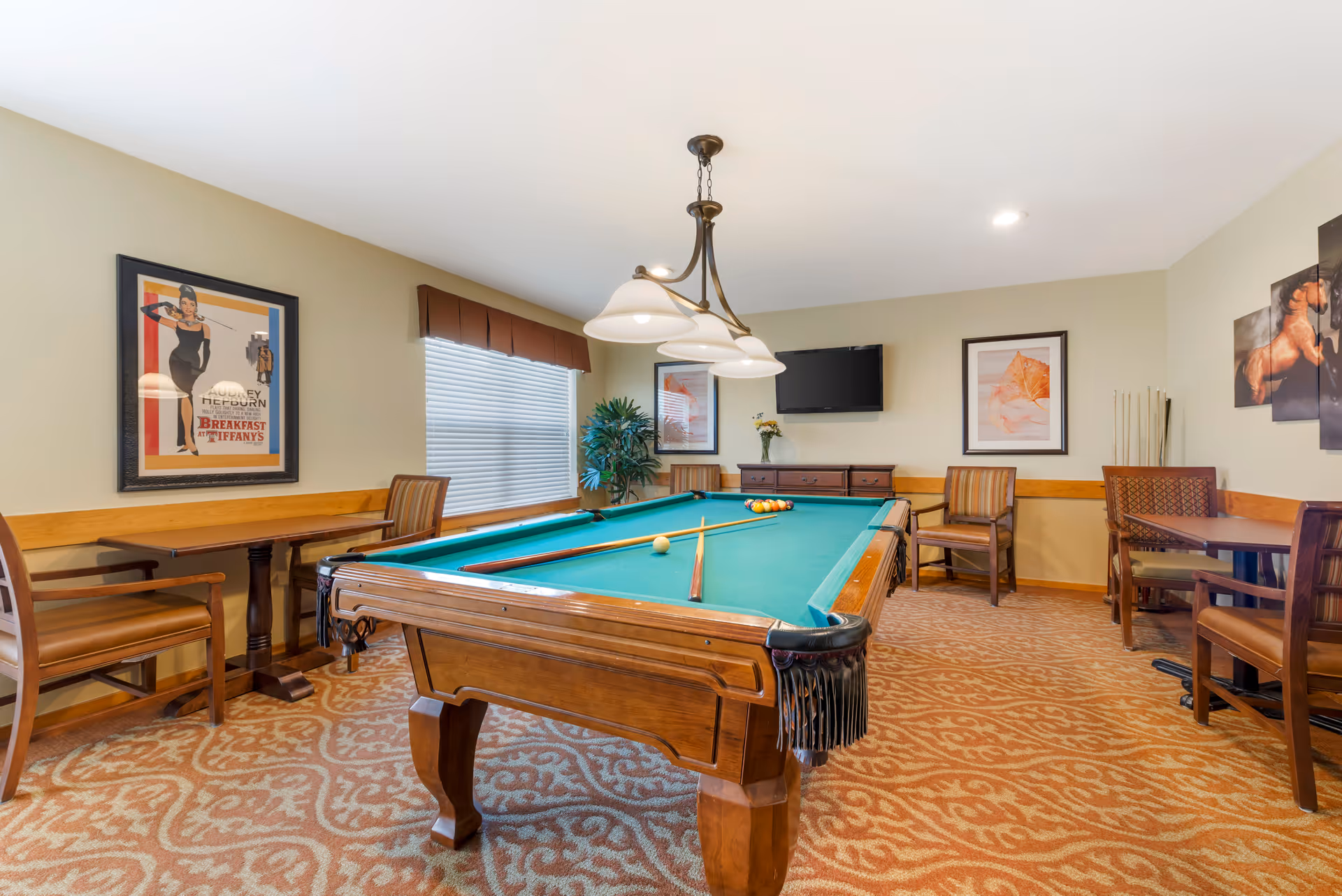 Well-lit interior game room with a pool table, seating, framed artwork, and a wall-mounted TV.