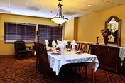 Formal dining room with a rectangular table set with napkins and place settings, wooden chairs, sideboard with mirror and flowers, chandelier, and windows with closed blinds.
