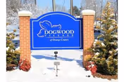 Blue sign for Dogwood Village of Orange County mounted on two brick pillars with snow on the ground and evergreen trees on either side.