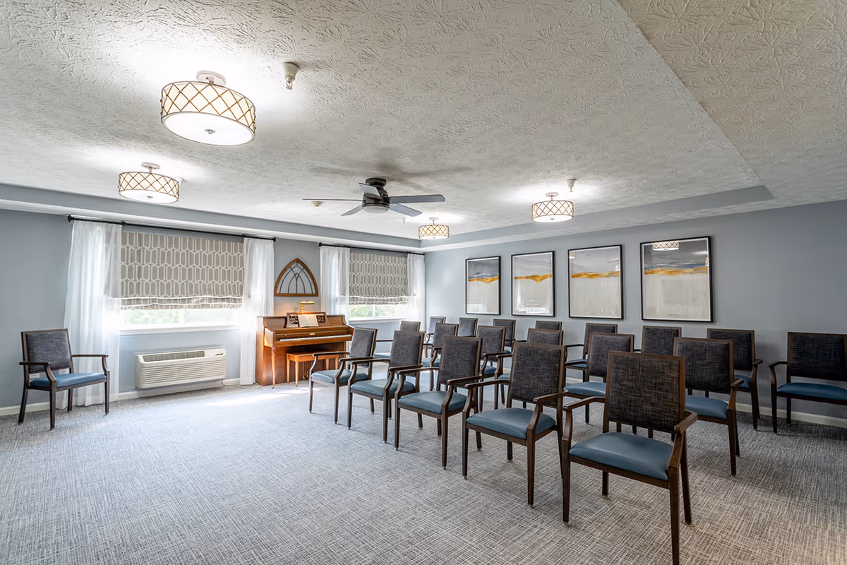 Bright common activity room with rows of chairs facing a piano beneath ceiling lights.