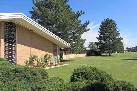 Front exterior view of Heritage Community/Dunaway Manor with lawn, shrubs, and tall trees.
