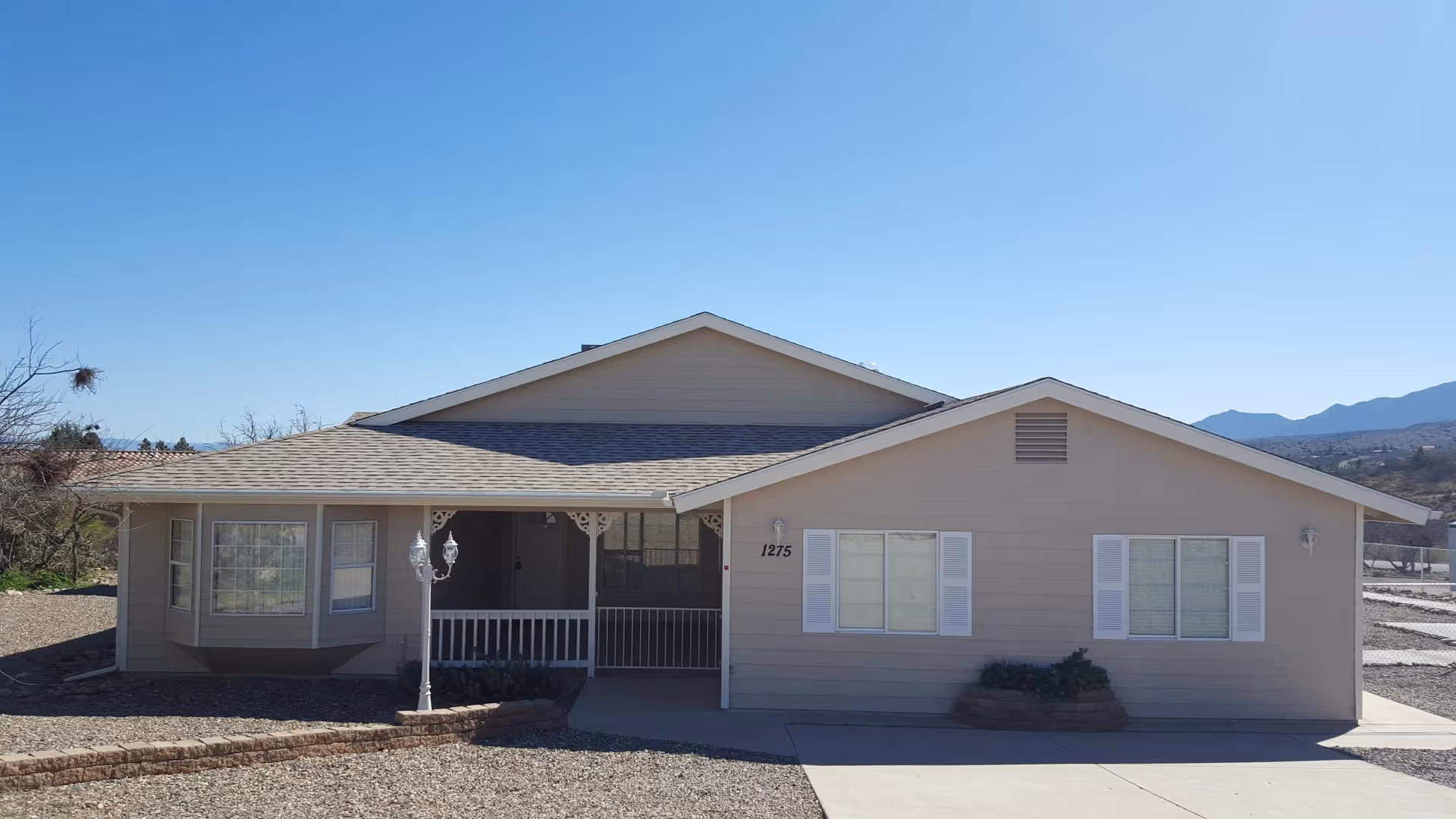 Front exterior of a single-story beige senior living building with a covered porch and visible house number 1275 against a clear blue sky.