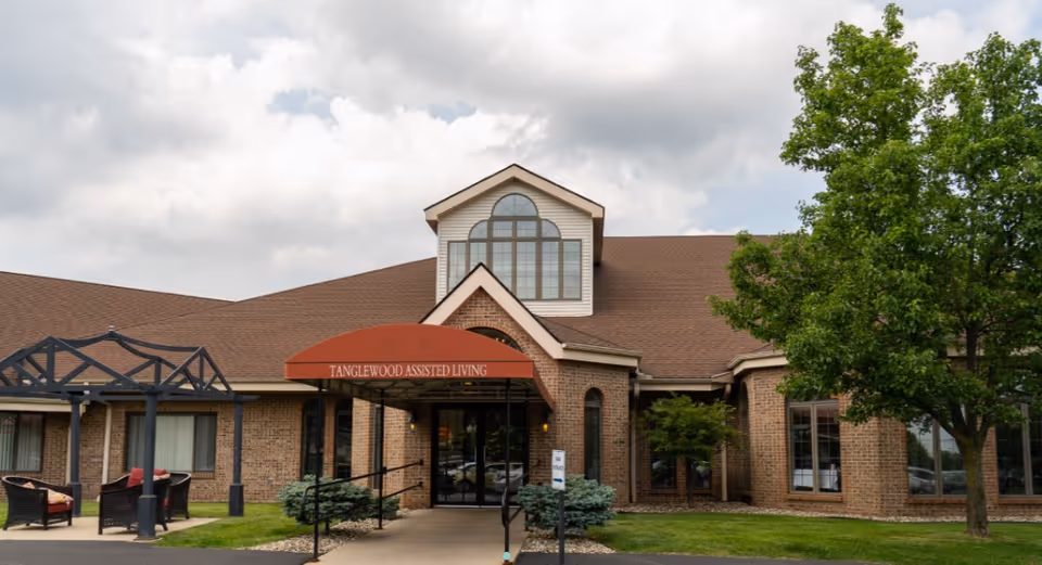 Front exterior of Tanglewood Assisted Living with entrance, red awning, and outdoor seating.