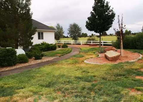 Curved walkway winds through a landscaped outdoor area toward a small white building.