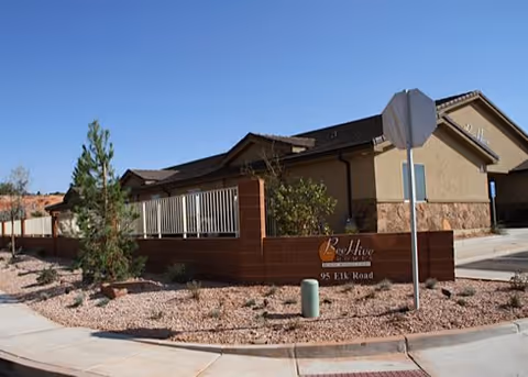 Exterior front view of a single-story Beehive senior living building behind a low brick wall with desert landscaping and a sign reading 'BeeHive 95 Elk Road'.