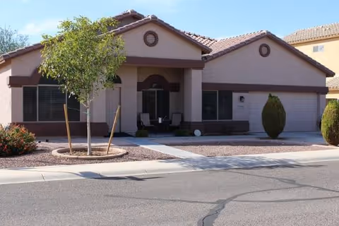 Front view of a beige, single-story senior care facility with a driveway and trees.