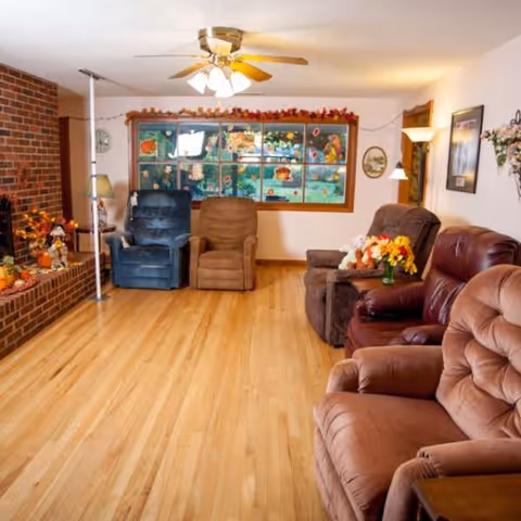 Cozy senior living living room with recliners, wood floors, brick accent, and decorative display cabinet.