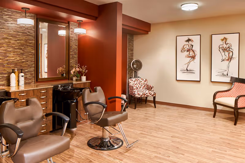 Salon-style room with styling chairs, sinks, mirrors, and additional seating against warm red and beige walls.