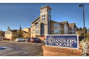 Front exterior of Chandler's Square Retirement Community featuring a sign, brick building, and parked cars.