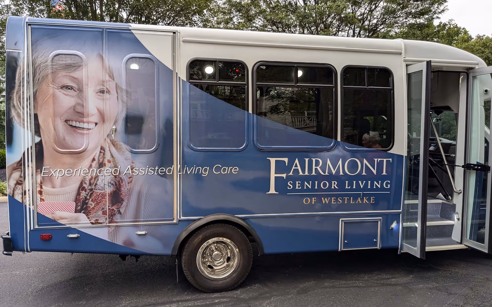 Side view of a Fairmont Senior Living shuttle bus with branding and a smiling elderly woman's portrait on the side.