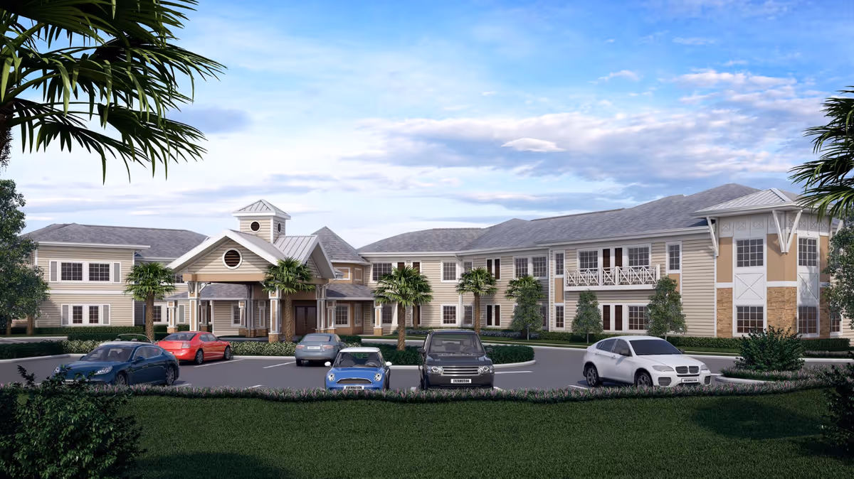 Two-story assisted living building with a covered main entrance, palm trees, landscaping, and several cars parked in front under a blue sky.