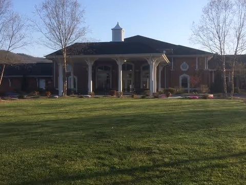 Front exterior view of a large brick building with a covered entrance supported by columns, surrounded by a well-maintained lawn and a few leafless trees under a clear blue sky.