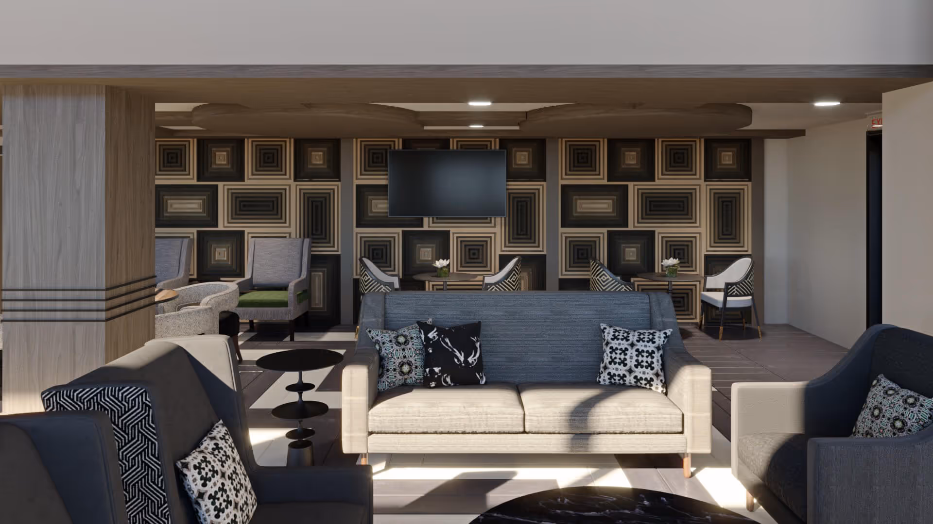 A modern living room area with a beige sofa and two dark armchairs, each with patterned throw pillows. Behind the sofa, there are additional seating areas with chairs and small tables. The back wall features a geometric patterned design in neutral tones and a mounted flat-screen TV. The room has a clean, contemporary look with soft lighting.