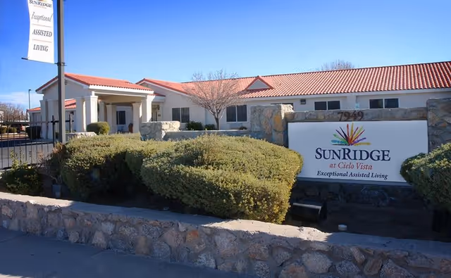 Front exterior of an assisted living facility with a sign reading 'SunRidge at Cielo Vista', red tile roof, entrance portico, and landscaped shrubs.