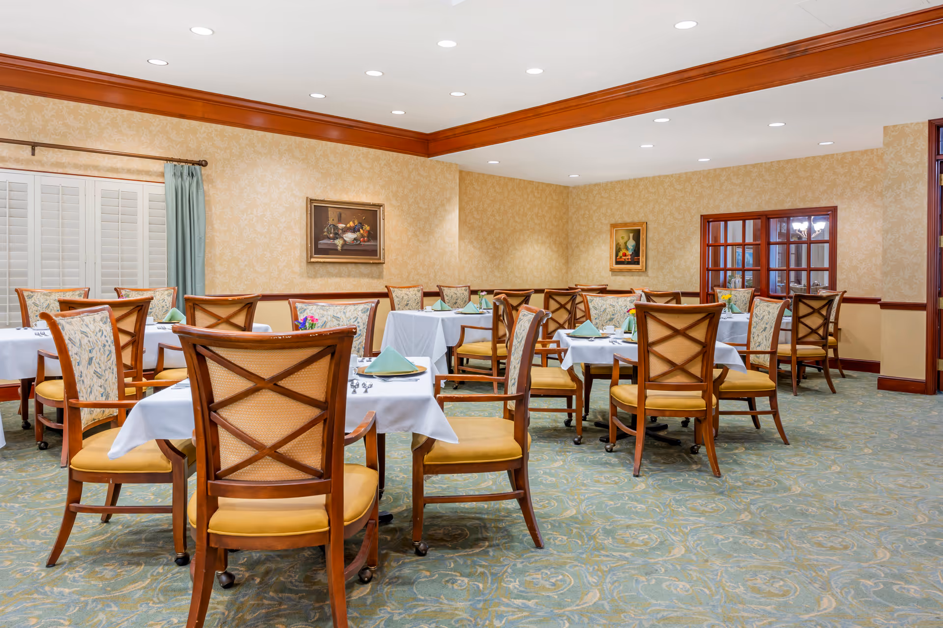 Bright dining room with multiple tables set with white linens, wooden chairs, and folded napkins.