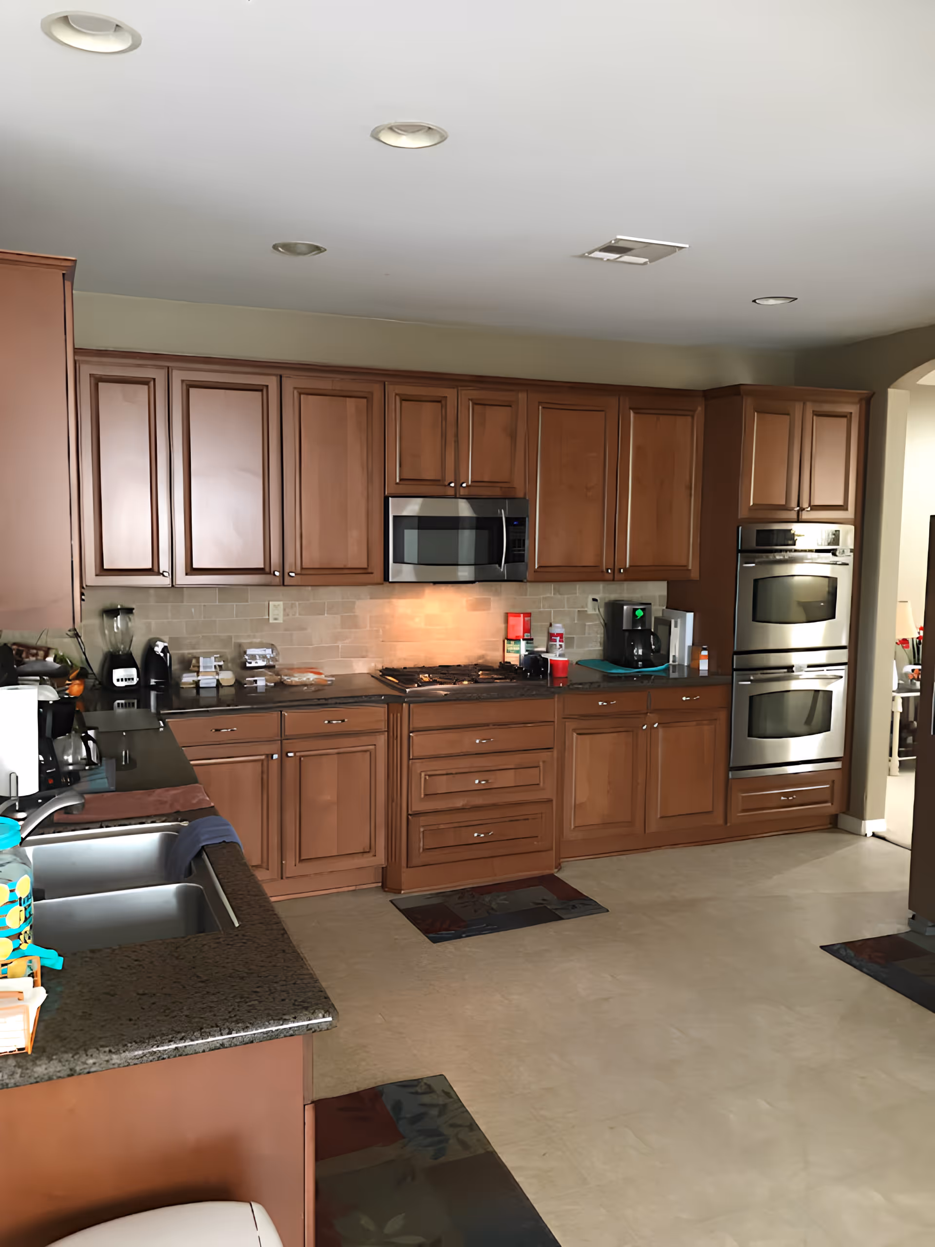 Bright kitchen with wooden cabinets, stainless steel double oven and microwave, gas cooktop, sink, and granite countertops.