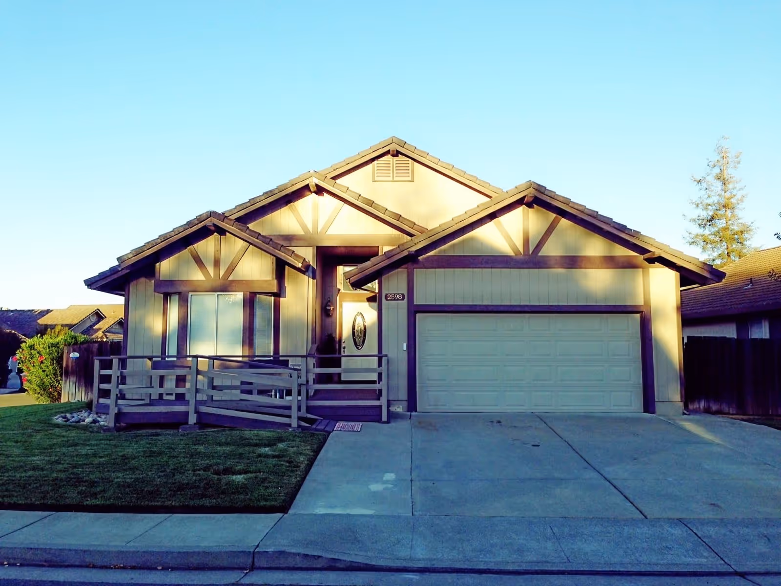 Front exterior view of a single-story residential house with a two-car garage, a small ramp leading to the front door, and a well-maintained lawn under a clear blue sky.