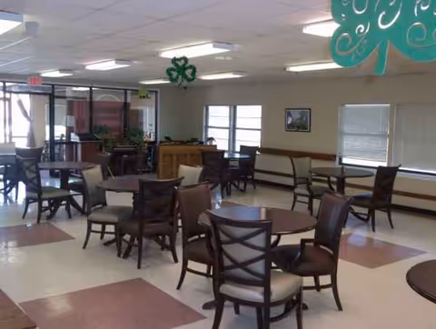 Empty dining room with round tables, cushioned chairs, and green decorative swirls overhead.