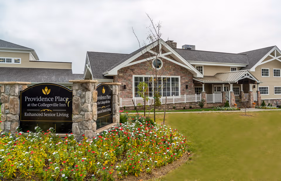 Exterior view of Providence Place at the Collegeville Inn, featuring a stone facade, landscaped garden with flowers, and a welcoming entrance.